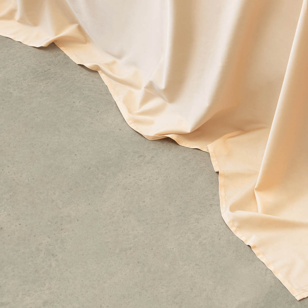 Close-up of peach-colored sheet fabric cascading smoothly onto a light gray concrete floor