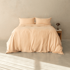 Peach-colored quilt cover set made up on a double bed with two matching pillowcases against a neutral concrete wall