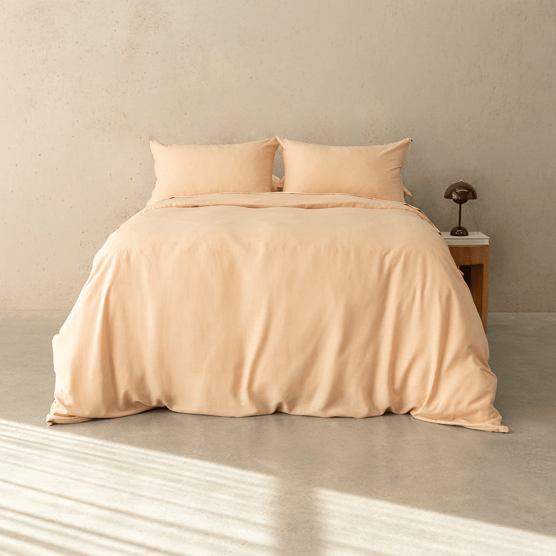 Peach-colored quilt cover set made up on a double bed with two matching pillowcases against a neutral concrete wall