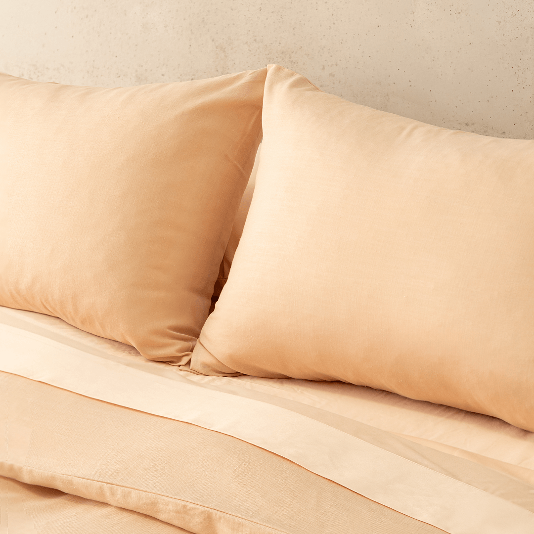 Close-up view of two peach pillowcases leaning against a matching flat sheet