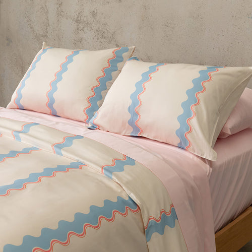 Bed with pink and blue striped bedding and pillows against a gray wall.