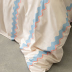 Close-up of a cream duvet cover with blue and pink zigzag trim on a neutral background.