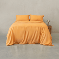 Mustard yellow quilt cover set made up on a double bed with two matching pillowcases against a concrete wall