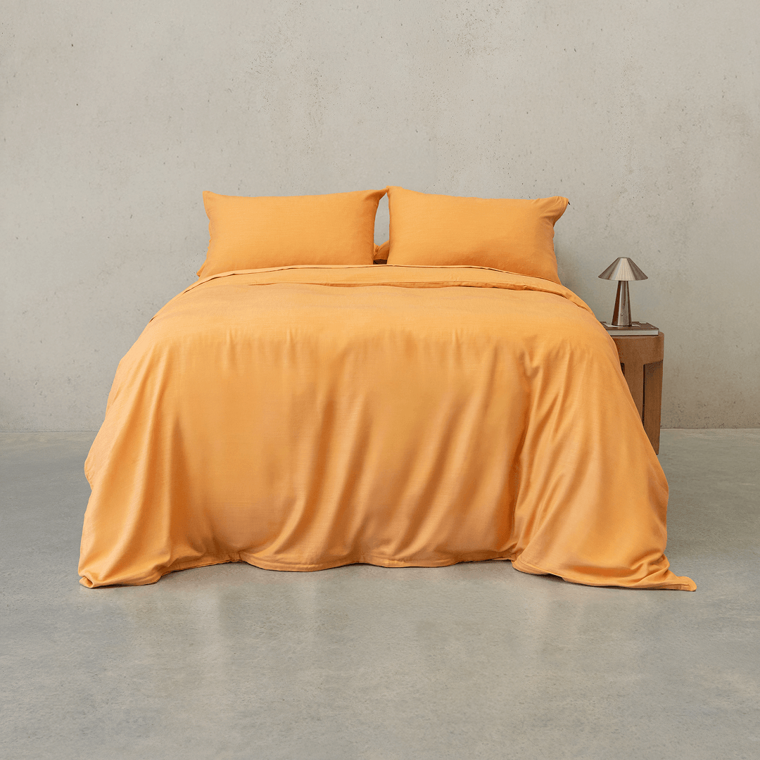 Mustard yellow quilt cover set made up on a double bed with two matching pillowcases against a concrete wall