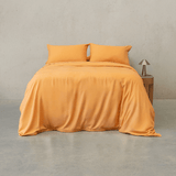 Mustard yellow quilt cover set made up on a double bed with two matching pillowcases against a concrete wall