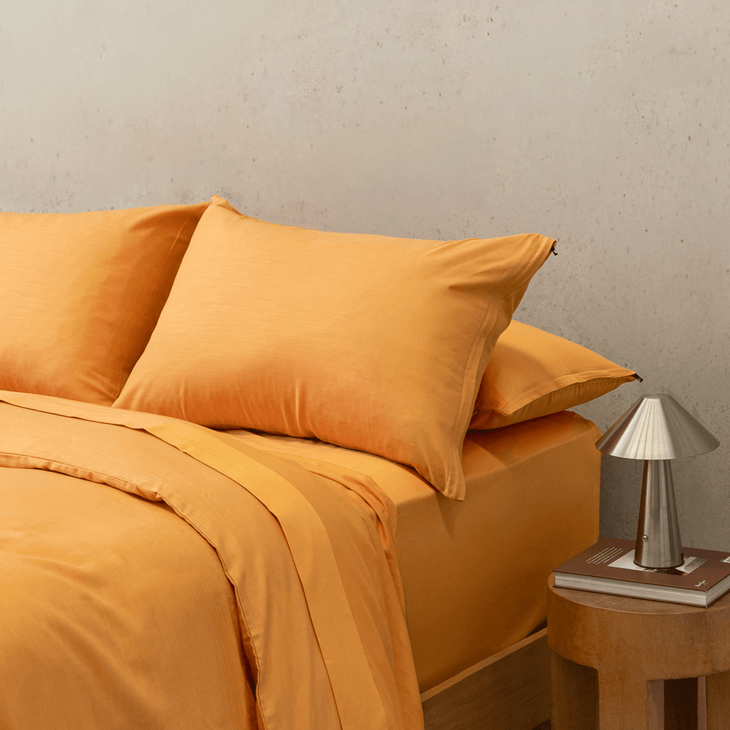 Side view of a double bed styled with a mustard yellow quilt cover, matching pillowcases, and a modern bedside lamp