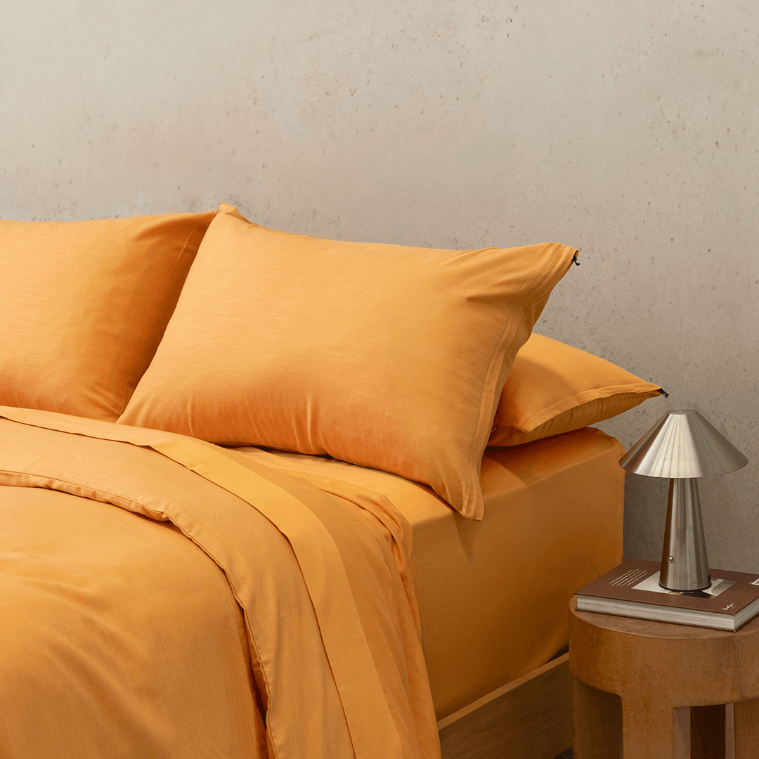 Side view of a double bed styled with a mustard yellow quilt cover, matching pillowcases, and a modern bedside lamp