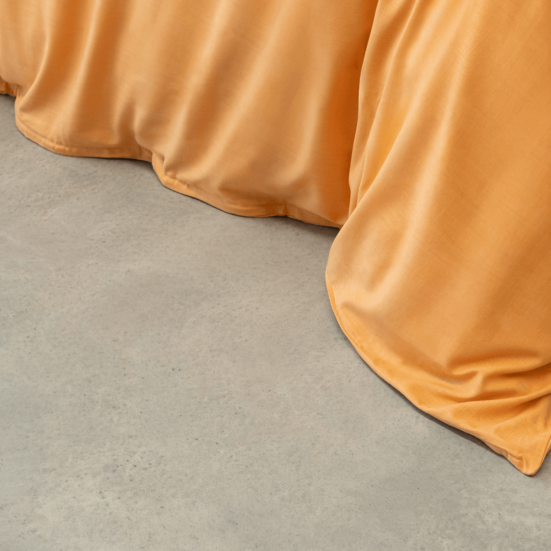 Close-up view of a mustard yellow quilt cover draping onto a light gray concrete floor