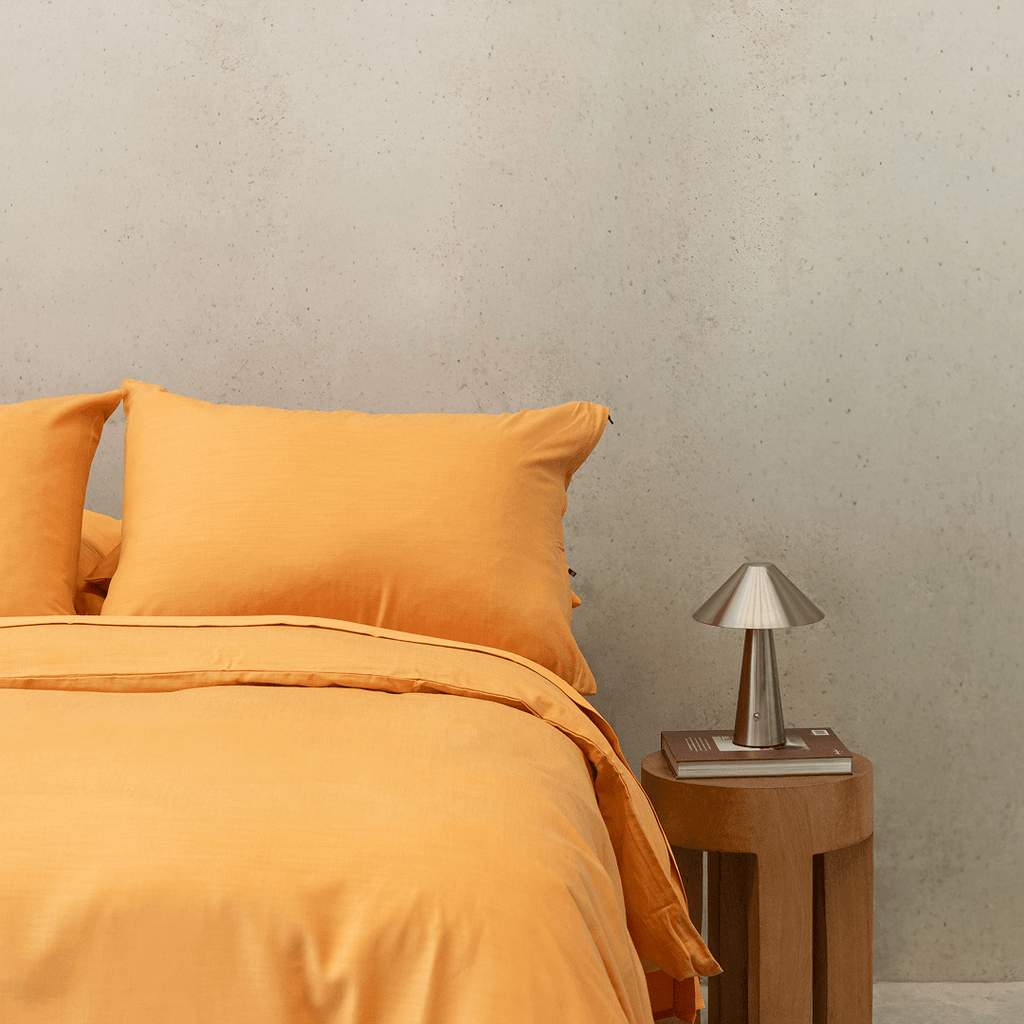 Styled bedroom scene featuring mustard yellow bedding alongside a wooden side table and metallic lamp