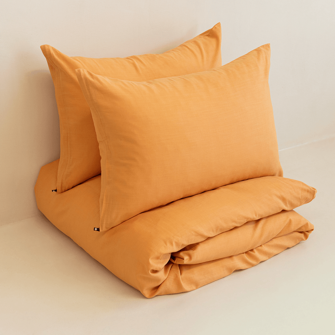 Neatly folded mustard yellow quilt cover with two matching pillowcases stacked on top
