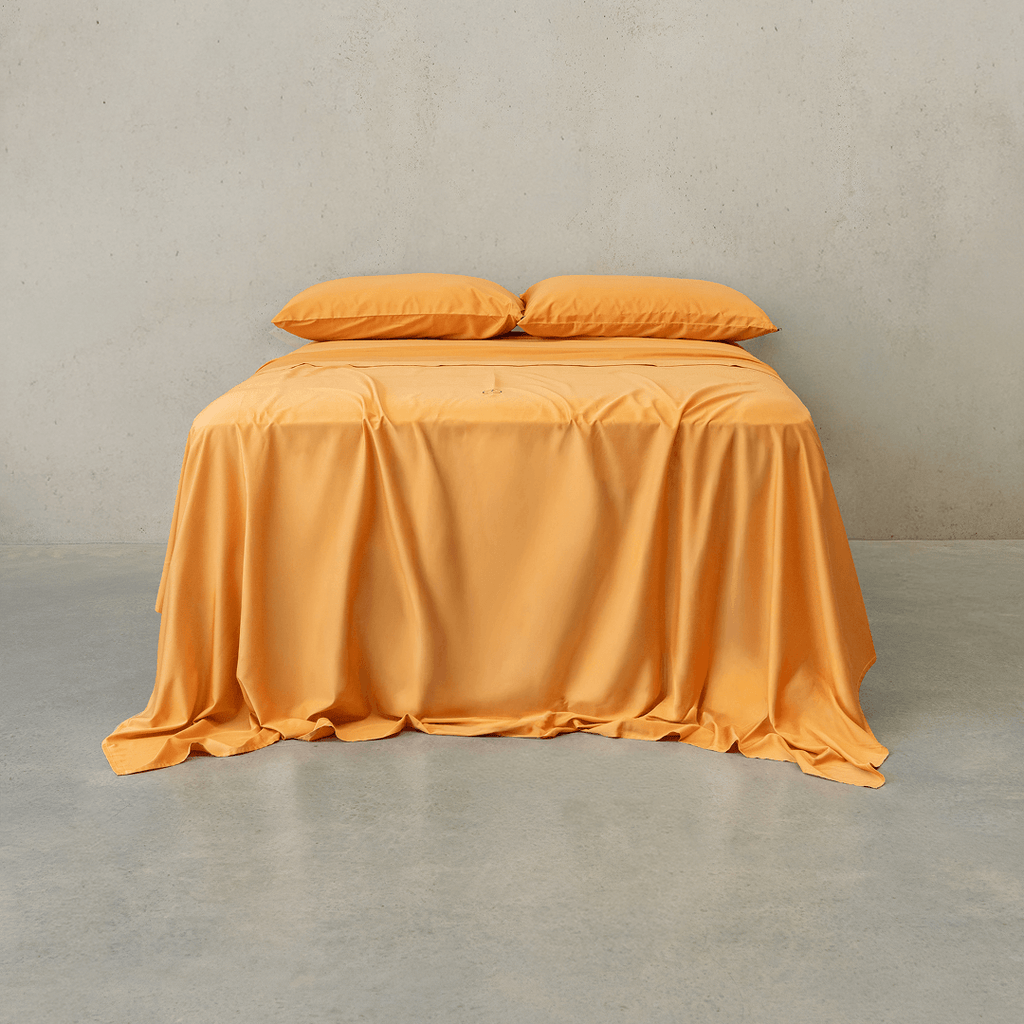 Mustard yellow bed sheet set draped over a double bed with two matching pillowcases against a textured wall