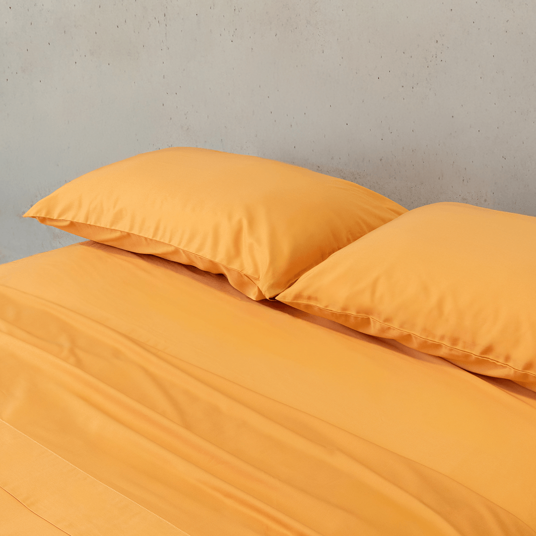 Mustard yellow bed sheet set draped over a double bed with two matching pillowcases against a textured wall