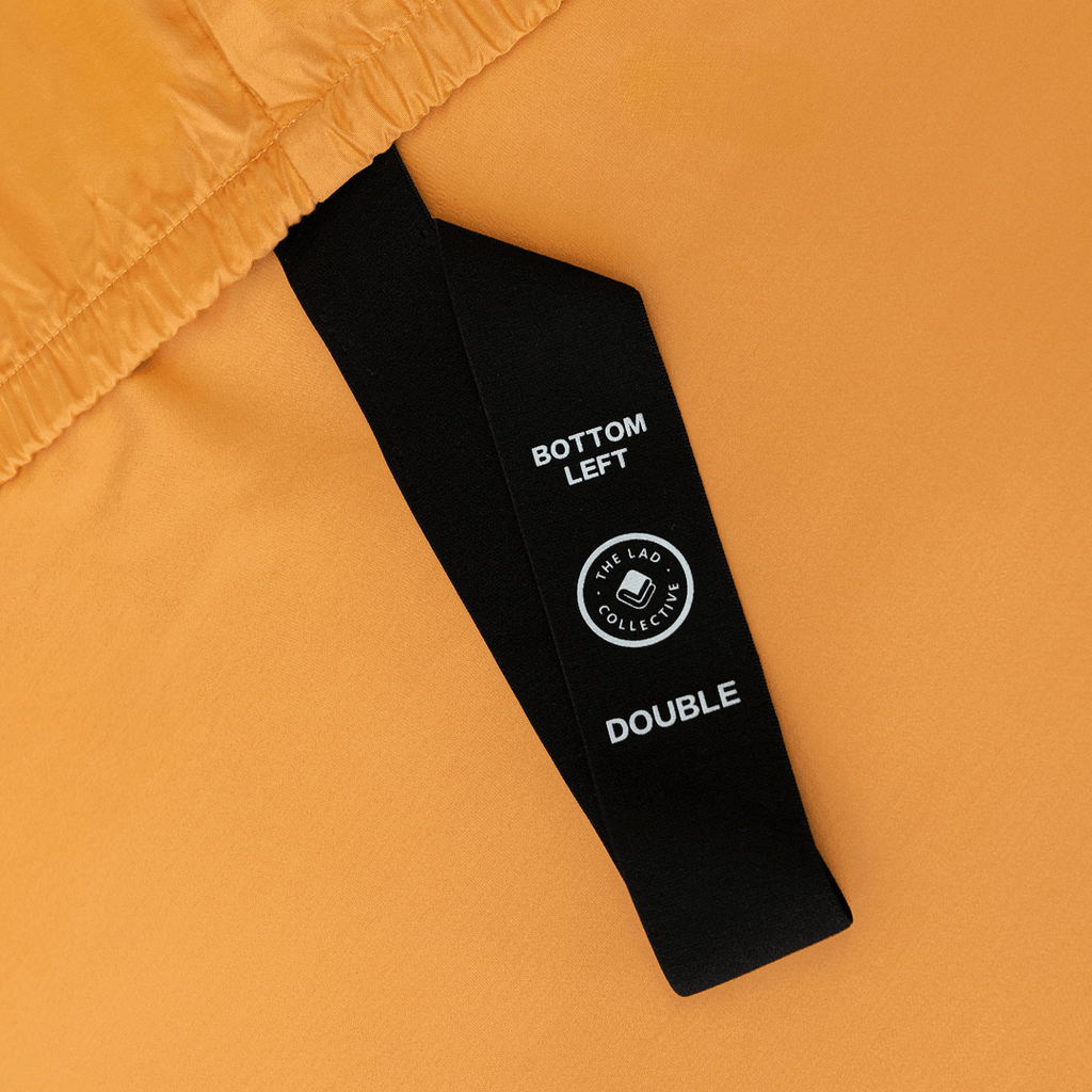 Close-up of a black corner elastic strap on a mustard yellow fitted sheet printed with 'Bottom Left' position label
