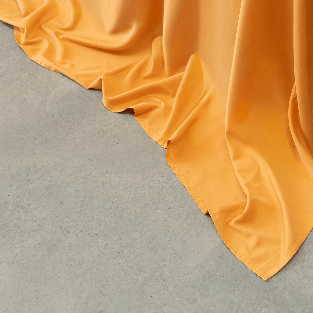 Close-up view of mustard yellow sheet fabric cascading smoothly onto a gray concrete floor