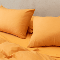Close-up angle view of mustard yellow pillowcases resting on a matching flat sheet