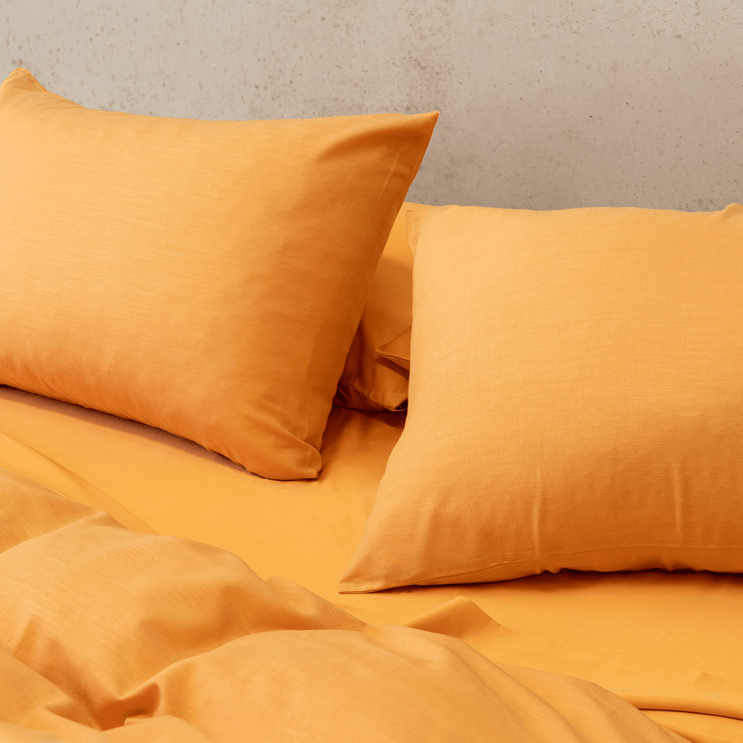 Close-up angle view of mustard yellow pillowcases resting on a matching flat sheet