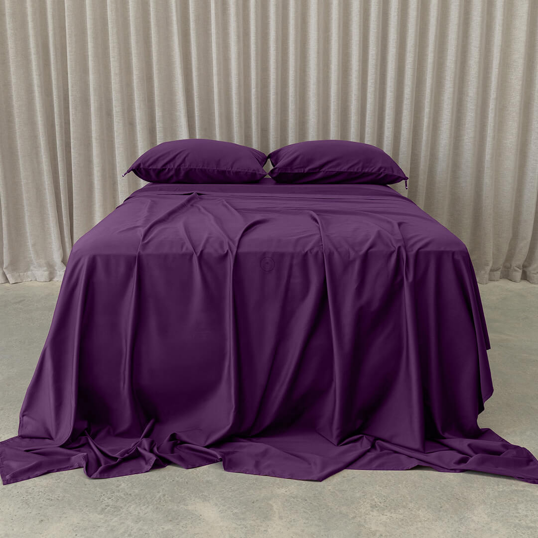 Deep purple bedding set on bed, in a neutral room. 