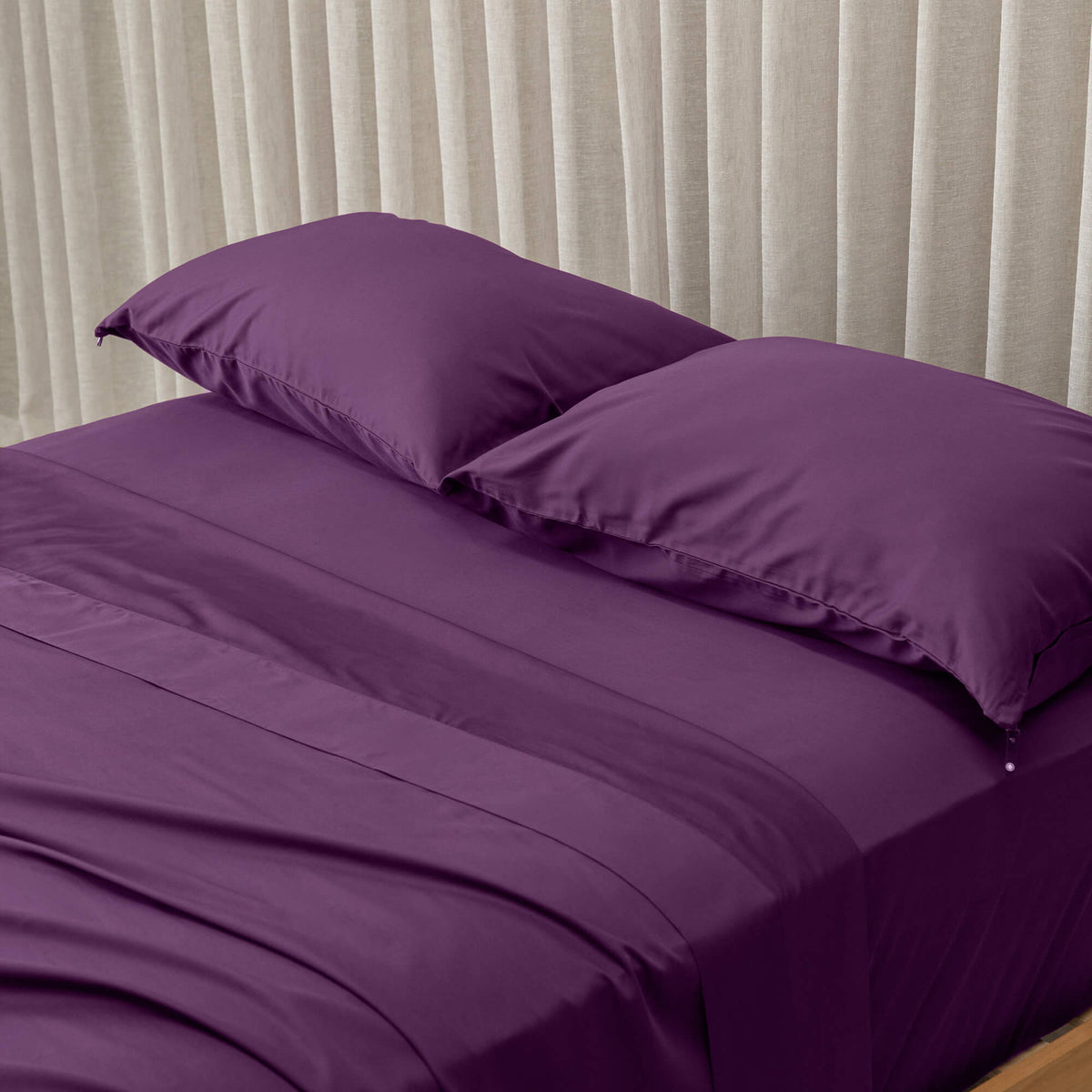 purple bedspread and pillows on a bed with beige curtains in the background
