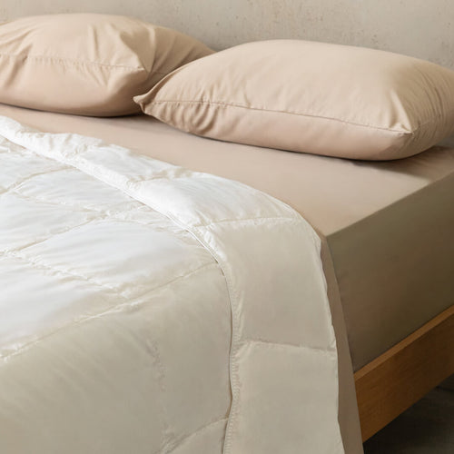 Beige bed with white quilt insert and pillows on a neutral background.