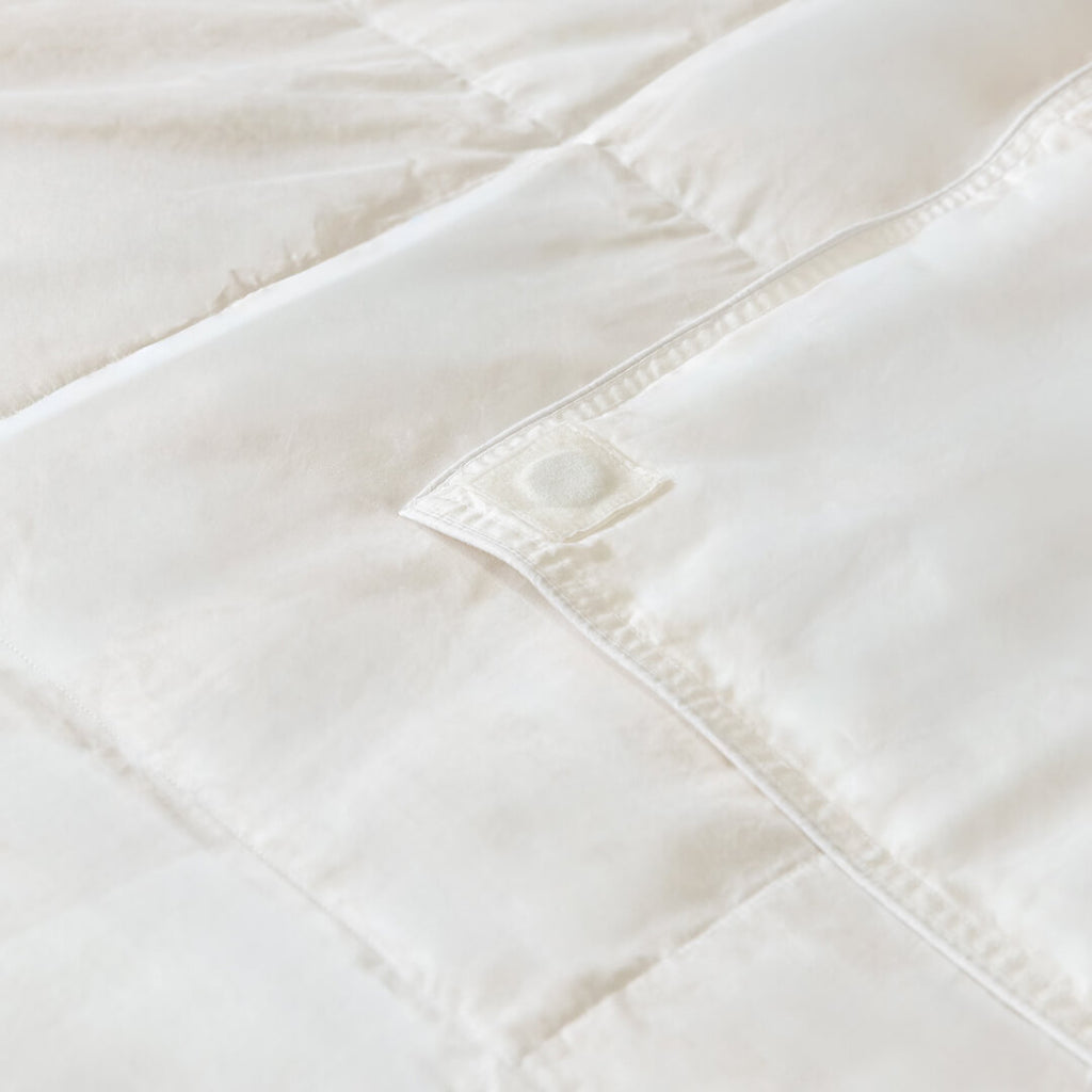 Close-up of a white quilted comforter with visible stitching on a light background.