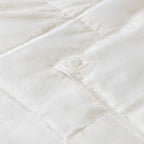 Close-up of a white quilted comforter with visible stitching on a light background.