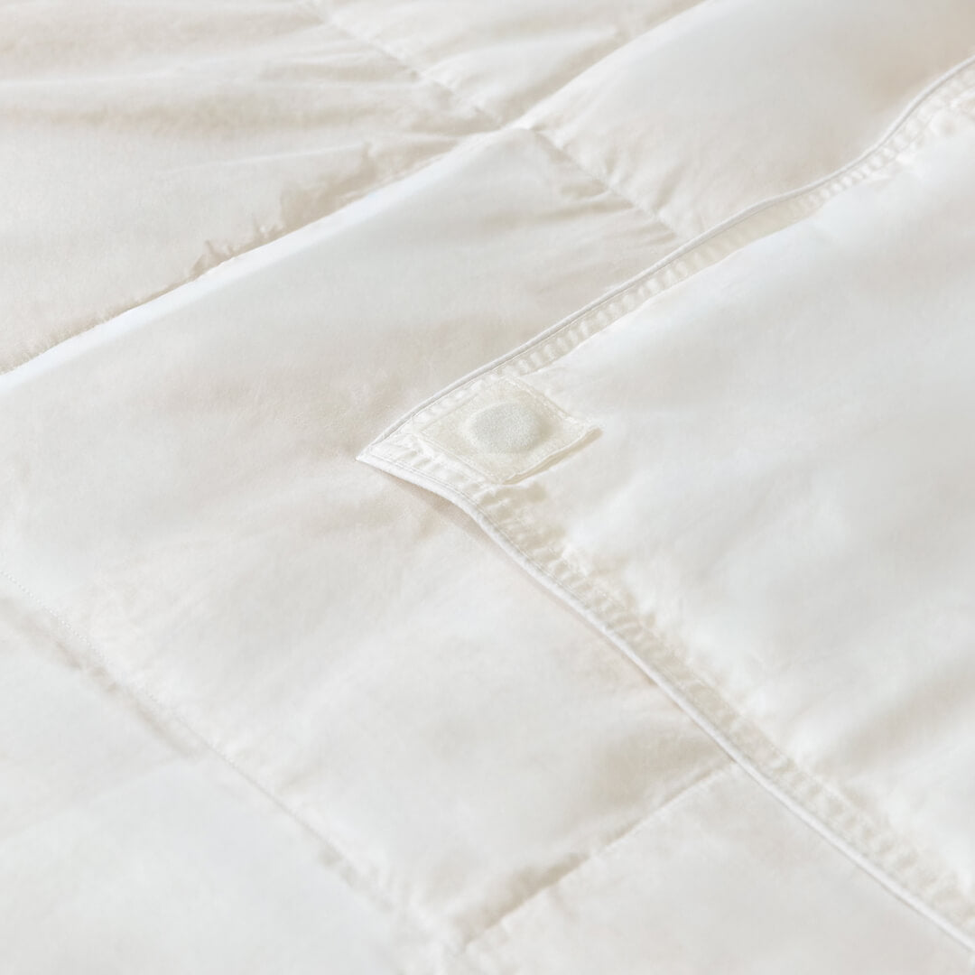 Close-up of a white quilted comforter with visible stitching on a light background.