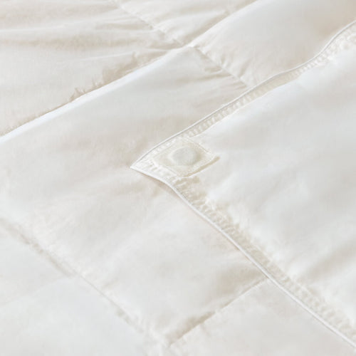 Close-up of a white quilted comforter with visible stitching on a light background.