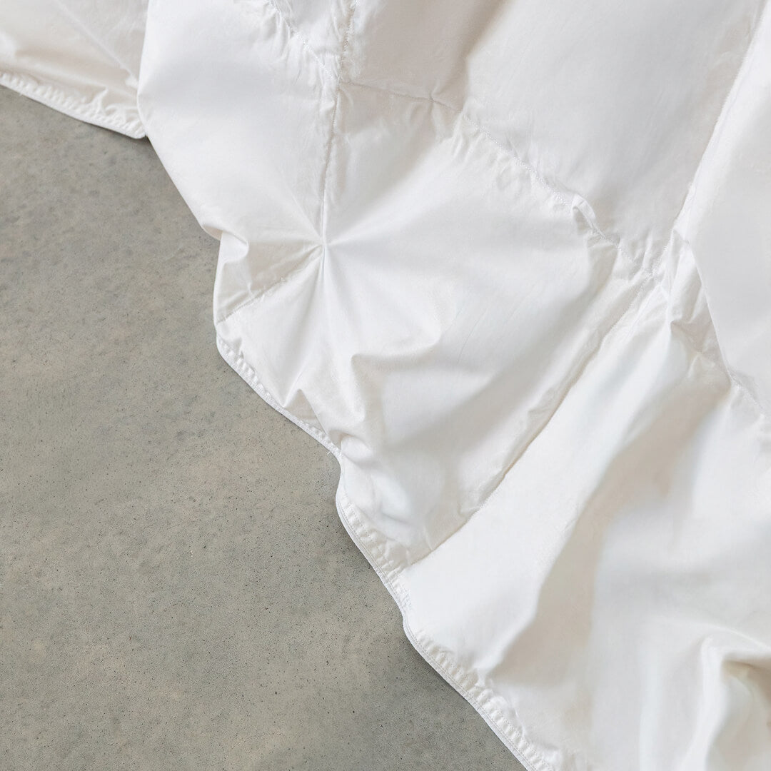 Close-up of a white lightweight quilt insert on a grey surface.