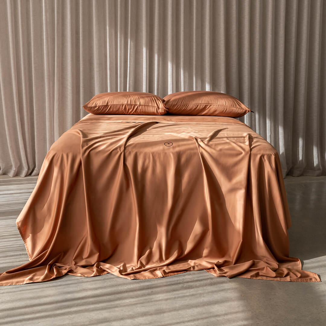 Brown bedspread on a bed with matching pillows against a neutral curtain background.