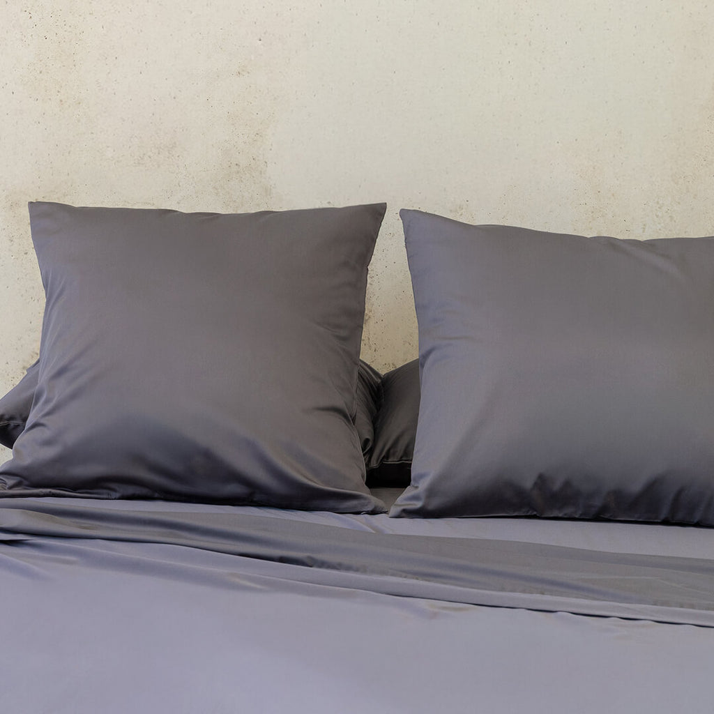 Grey bedding set with two pillows on a bed against a beige wall.