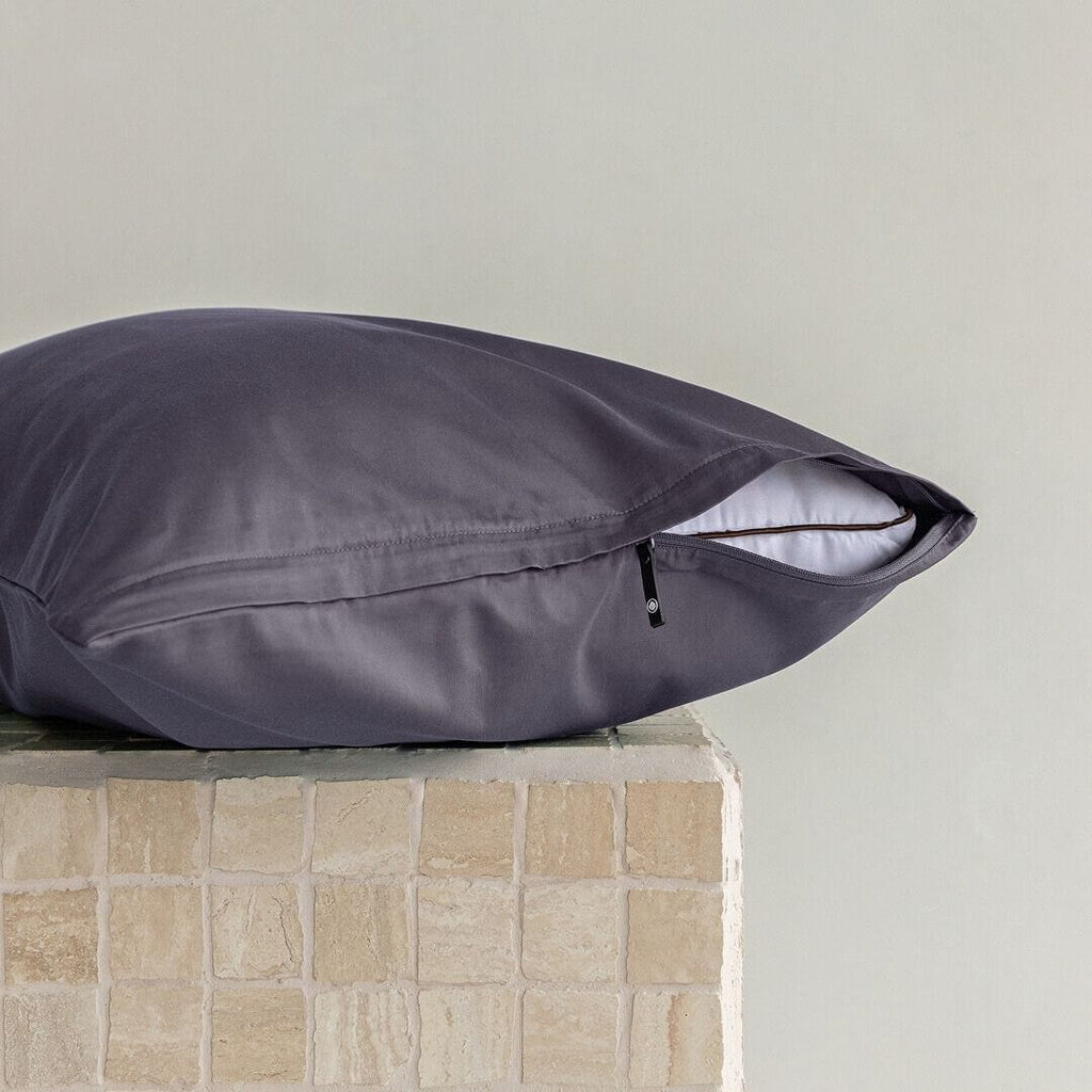 Dark grey pillow on a textured surface with a neutral background.