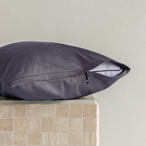 Dark grey pillow on a textured surface with a neutral background.