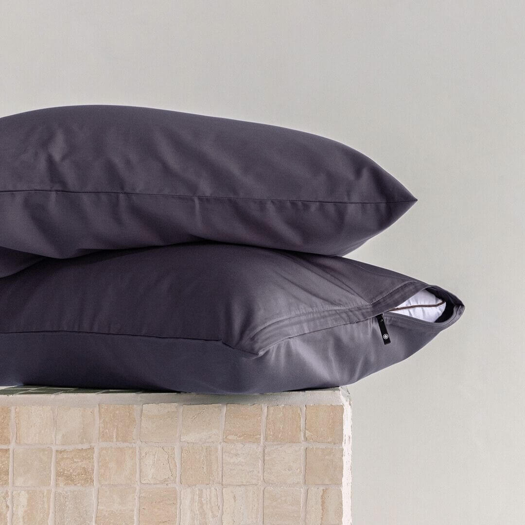 Two dark gray pillows stacked on a light-colored surface with a neutral background