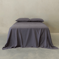 Charcoal grey fitted sheet set styled on a neatly made bed with matching pillowcases, showcasing a clean, modern bedroom aesthetic and soft fabric drape.