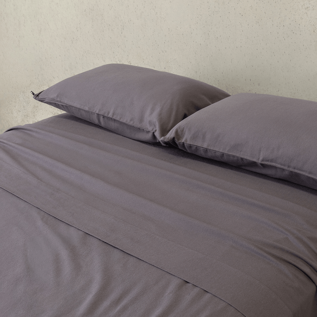 Close-up of a charcoal grey fitted sheet and matching pillowcases, highlighting the smooth texture, soft finish, and coordinated bedding design.