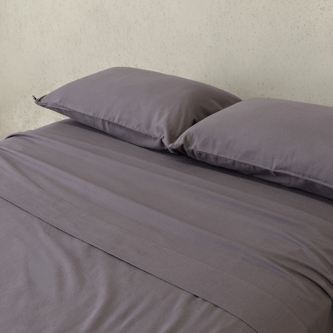 Close-up of a charcoal grey fitted sheet and matching pillowcases, highlighting the smooth texture, soft finish, and coordinated bedding design.