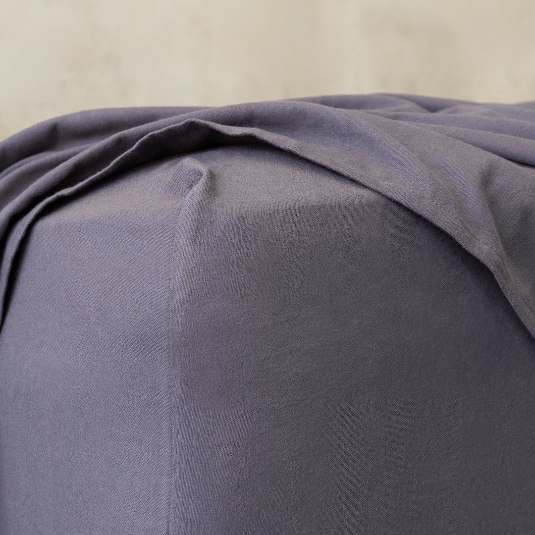 Close-up of a charcoal grey fitted sheet corner, highlighting the elasticized edge designed for a secure and snug mattress fit.