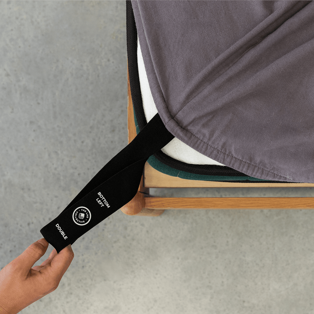 Charcoal grey fitted sheet with an orientation tag extended from the mattress corner, demonstrating the easy-to-identify labeling system for quick bed setup.
