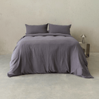 Front view of a bed dressed in dark stone gray bedding with two matching pillows and a relaxed quilt cover draped toward the floor.