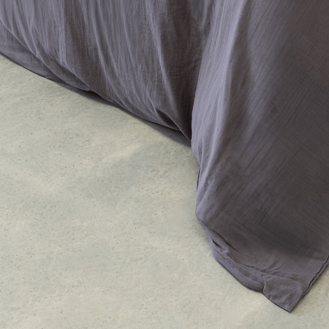 Close-up of a dark stone gray quilt cover draping onto a concrete floor, showing its soft texture and relaxed finish.