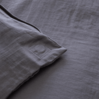 Close-up of the corner of a dark stone gray quilt cover showing a stitched square detail and textured stonewashed fabric.