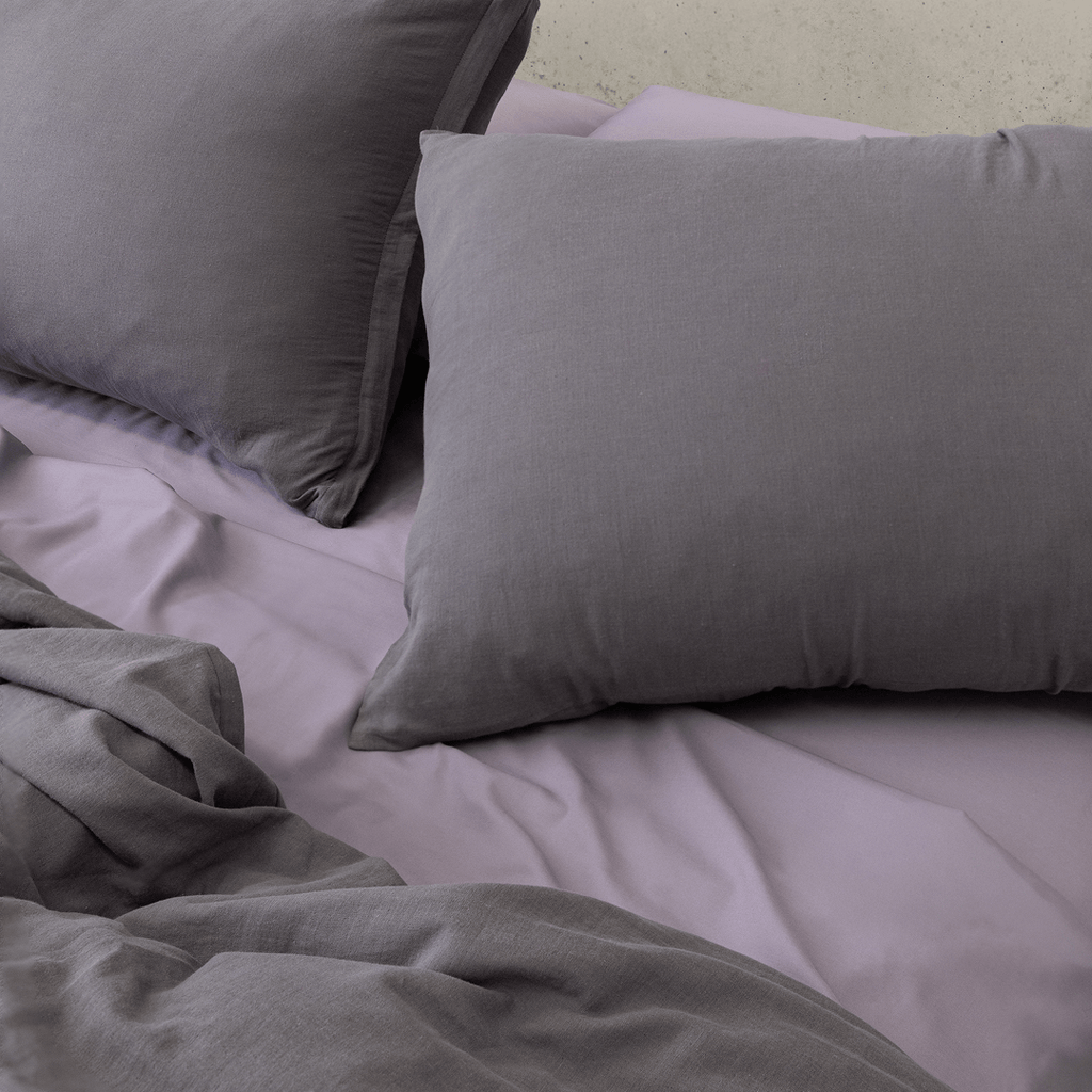 Close-up of dark stone gray pillows arranged over lighter gray bedding with the matching quilt cover softly gathered in front.
