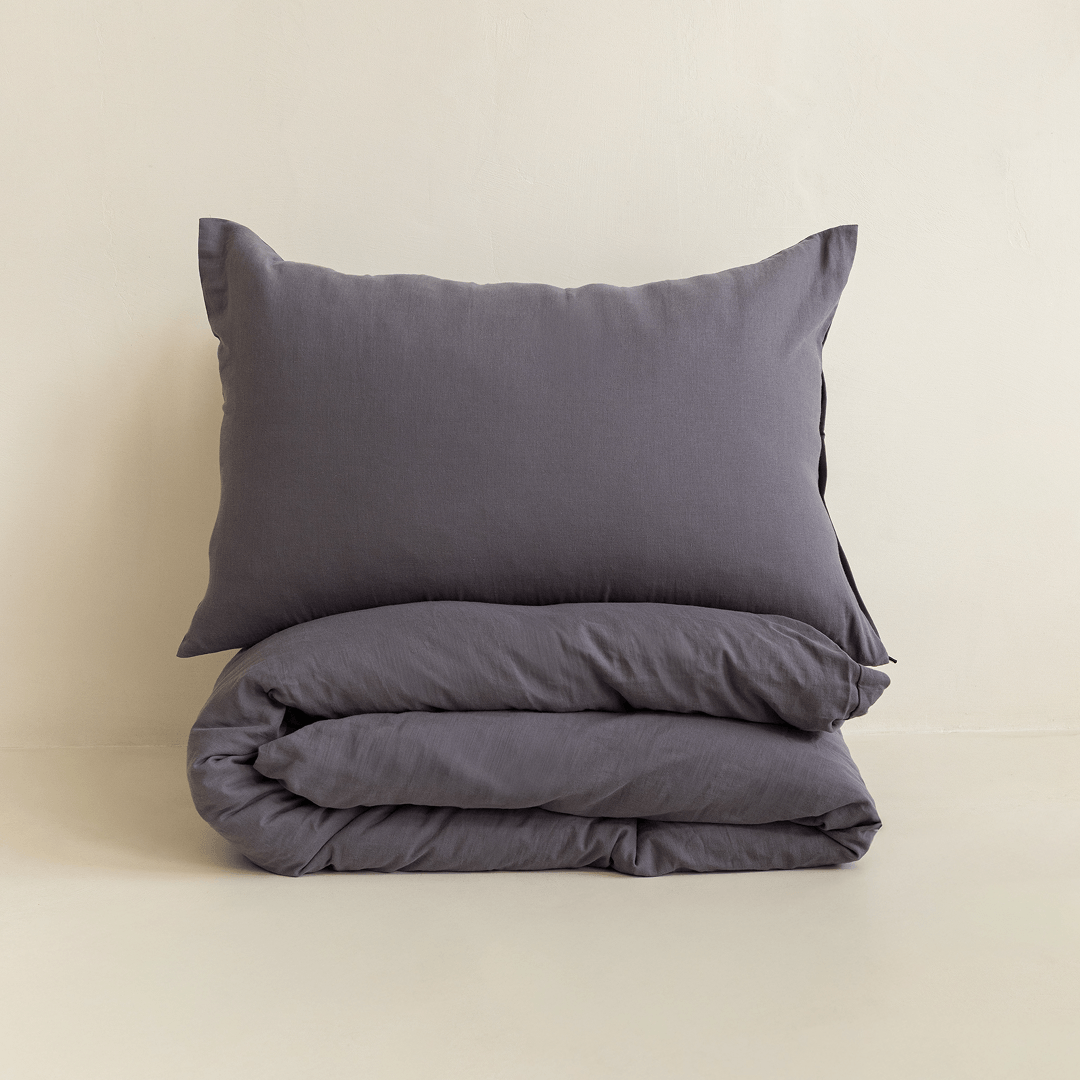 A dark stone gray pillow displayed above a neatly folded matching quilt cover against a warm neutral background.