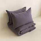 Two dark stone gray pillows arranged above a folded matching quilt cover in a minimal studio setting.