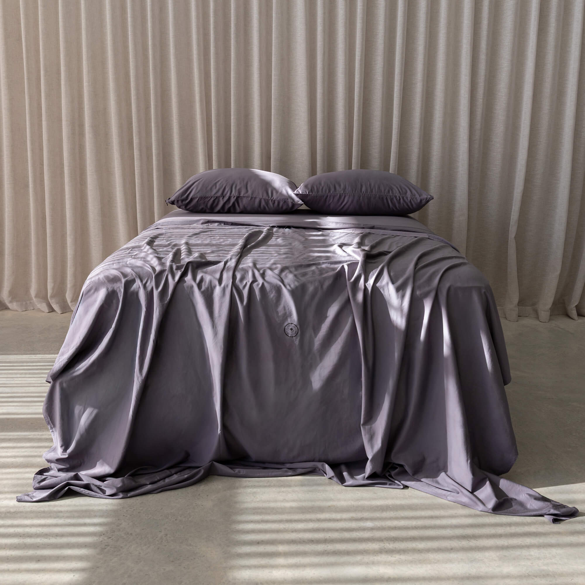 Bed with gray bedding and pillows against a beige curtain background