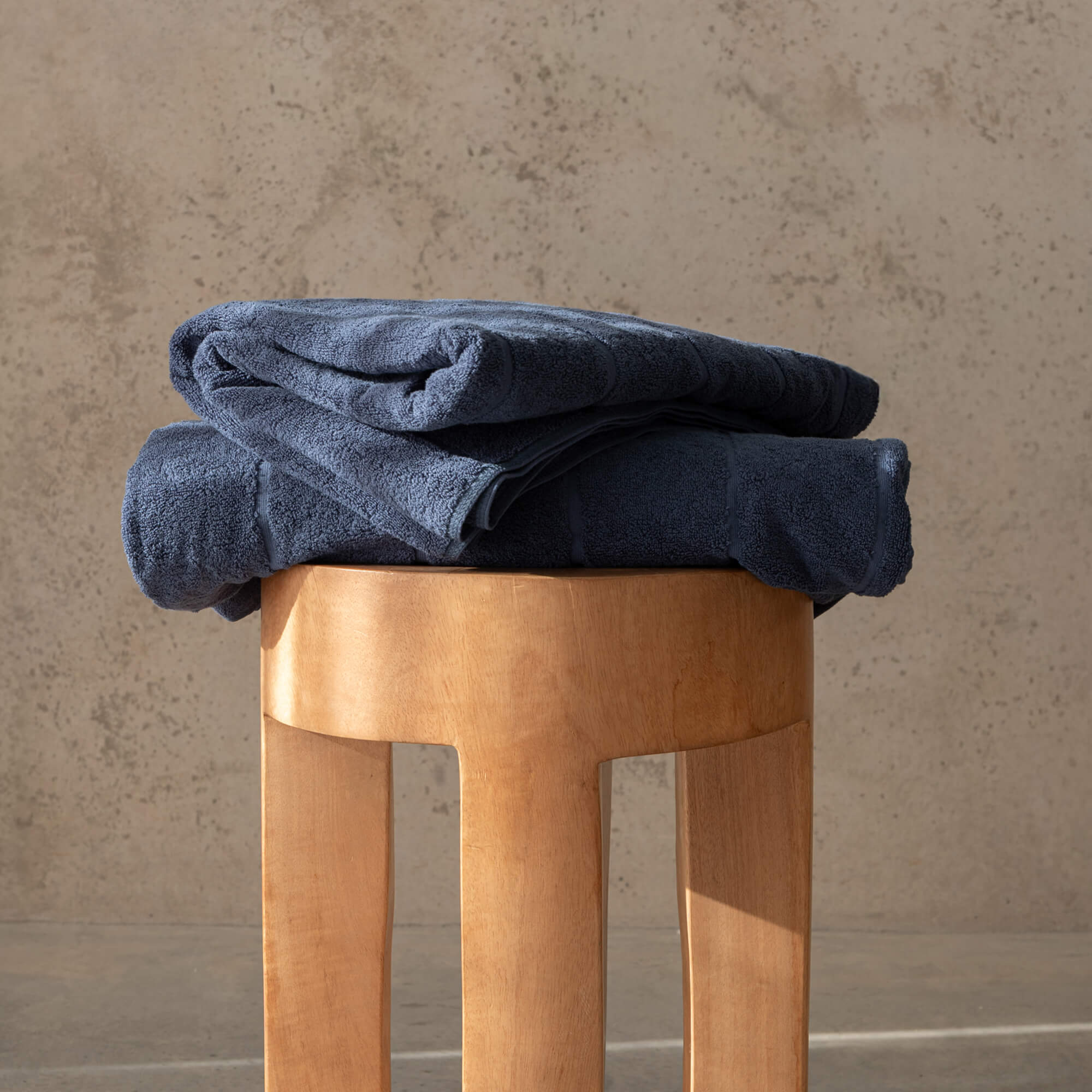 Folded blue towels on a wooden stool against a beige wall.