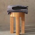 Folded gray towel on a wooden stool against a beige wall.