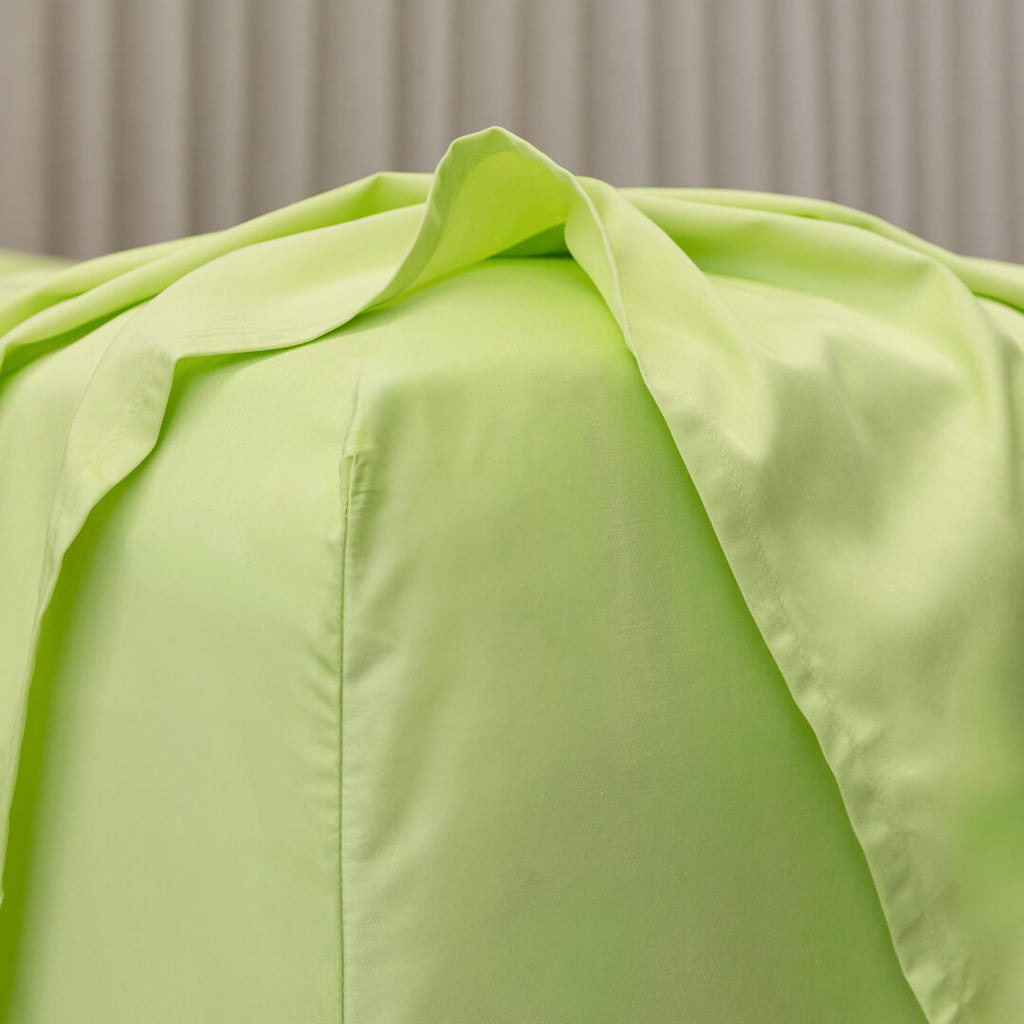 Close-up of a light green fitted sheet corner detail on a bed with a neutral background.