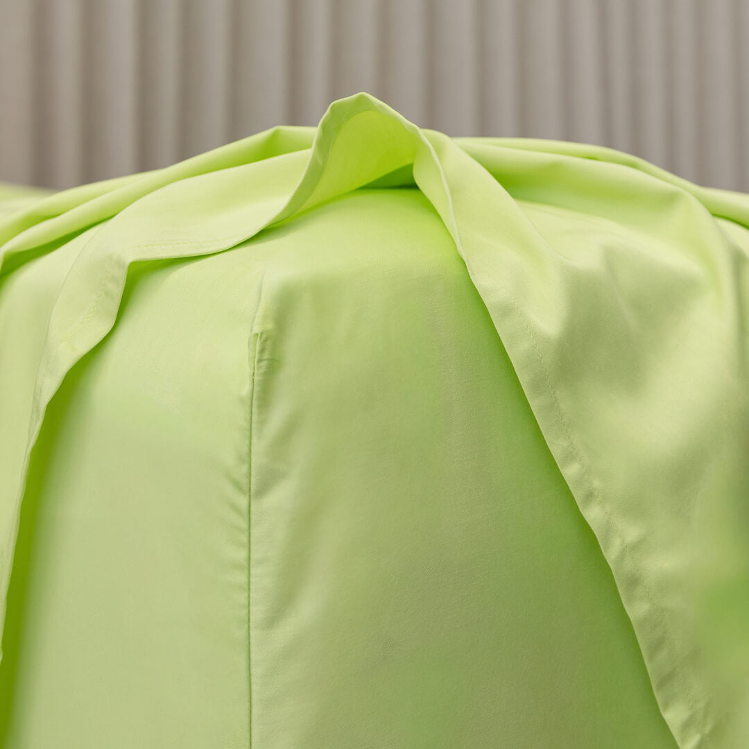 Close-up of a light green fitted sheet corner detail on a bed with a neutral background.