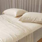 Cream bed sheets and pillows on a bed with a neutral headboard.